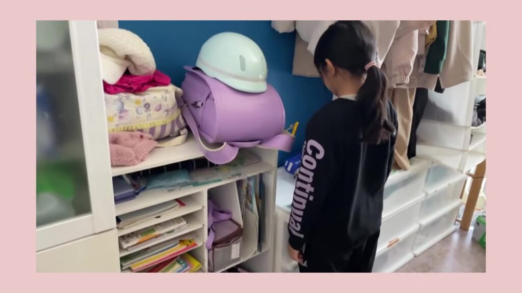 ランドセルラックの一番上にランドセルを置く小学生の娘